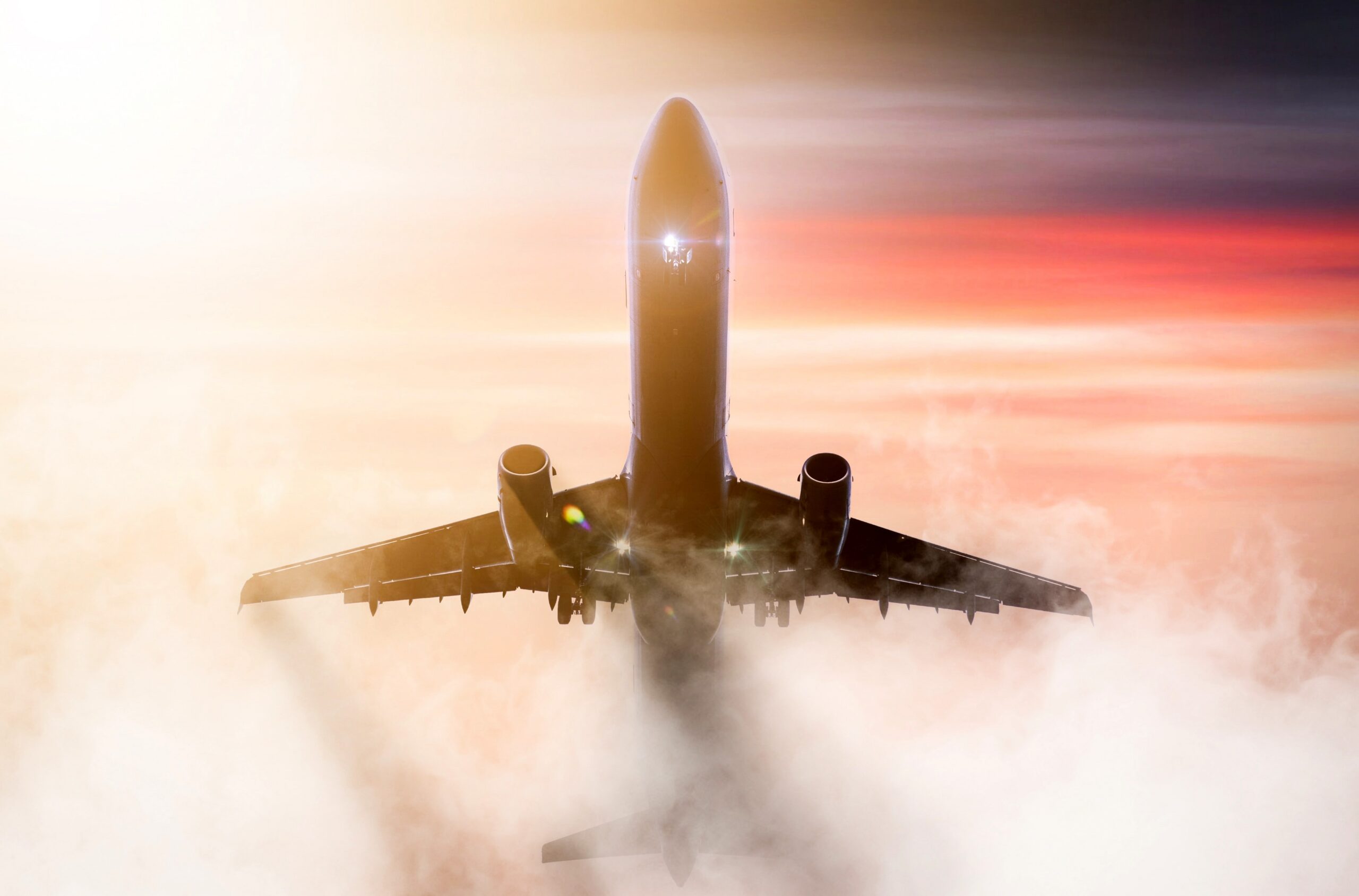 Twin engine passenger aircraft climbing through clouds at sunrise